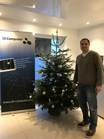 Sven Braun neben einem geschmückten Weihnachtsbaum, links ein Aufsteller von SB Computer