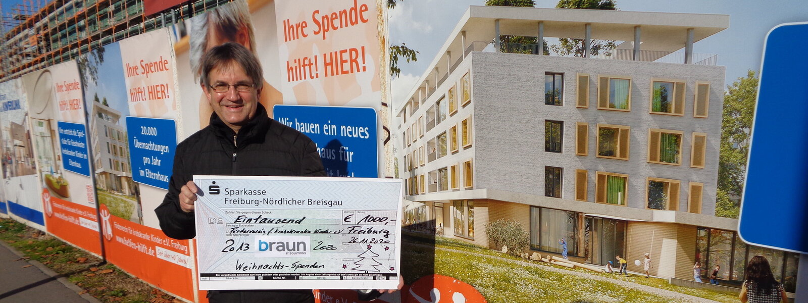 Der Spendenscheck 2020 vor dem Bauschild des neuen Elternhauses